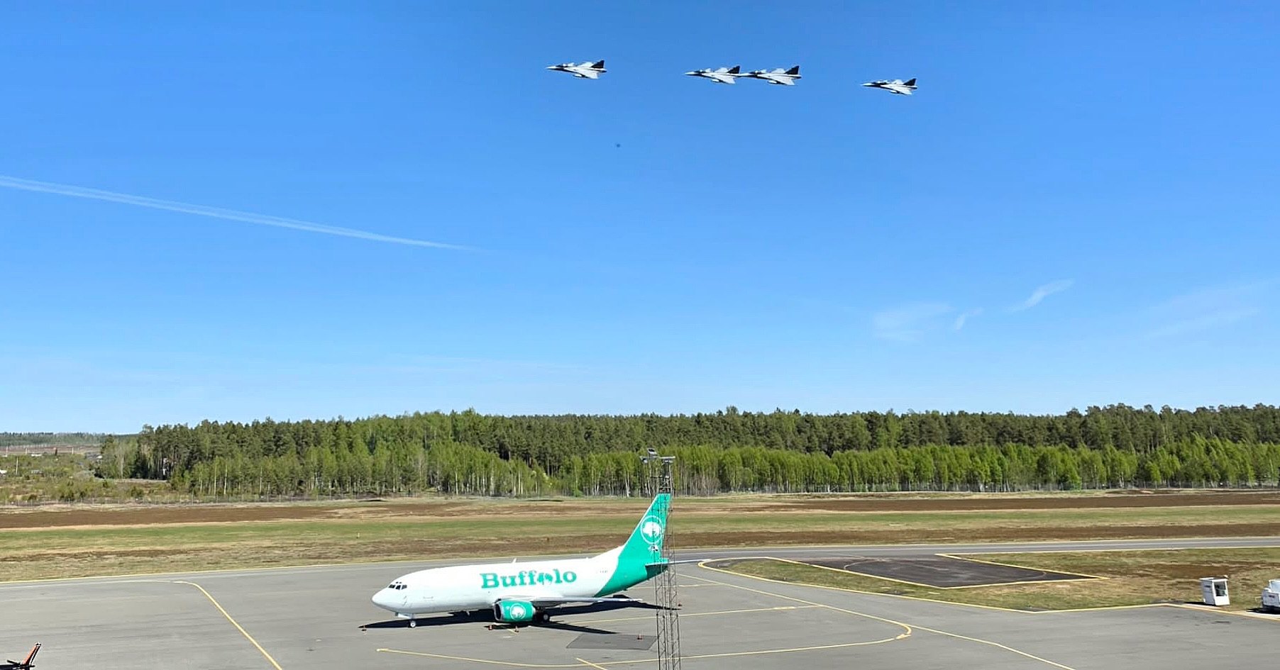 C-FBAE parked at Jönköping, Sweden, with a four-ship fighter formation overhead