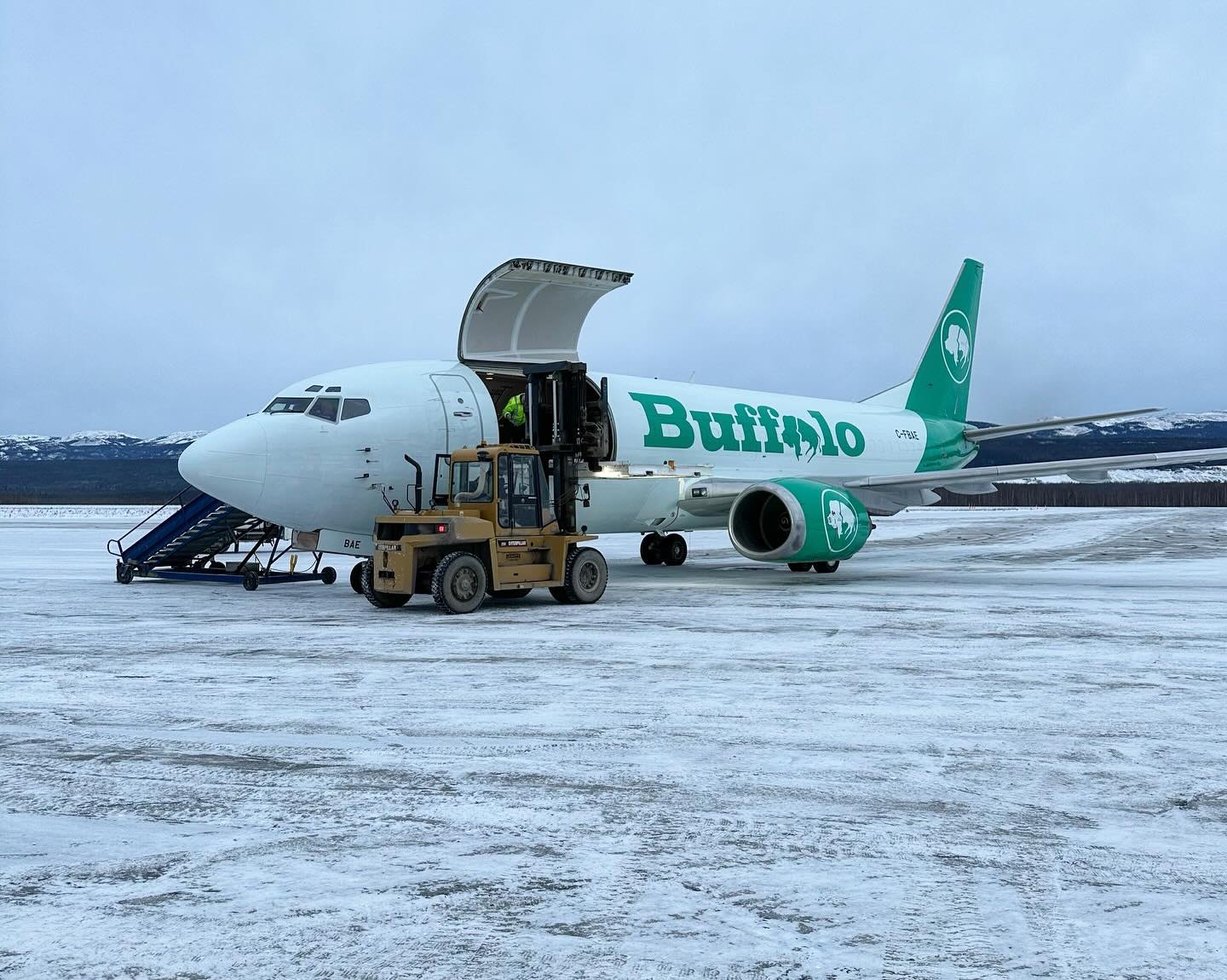Forklift unloading C-FBAE through the main deck cargo door on a snowy northern ramp