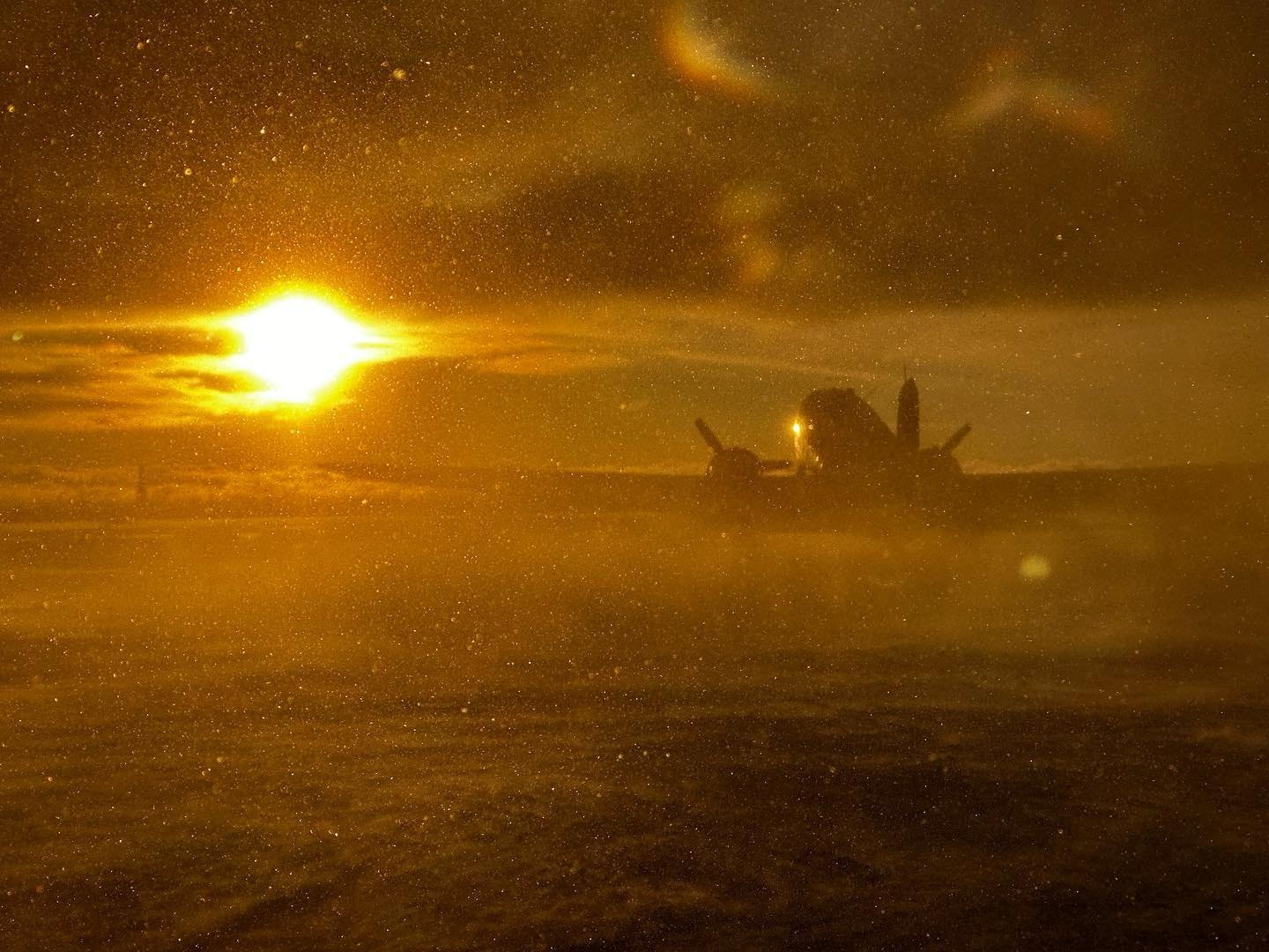 DC-3 silhouetted in golden blowing snow at sunset
