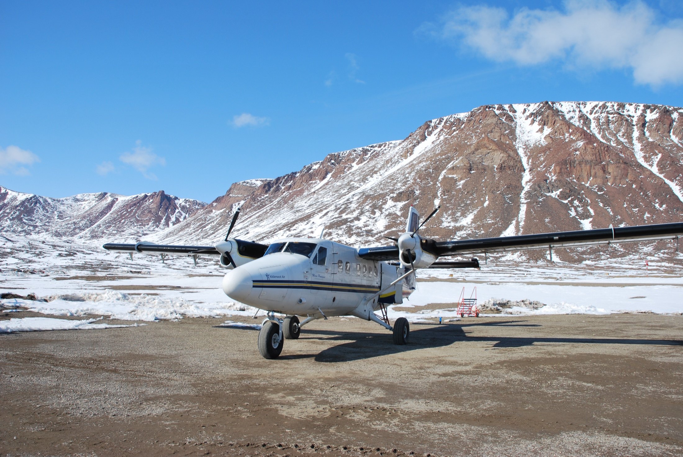 The Twin Otter on a dirt strip beneath snow-streaked red mountains